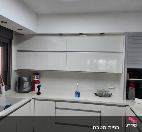 מטבח מודרני עם ארונות לבנים, מכשירים וכלי ניקוי